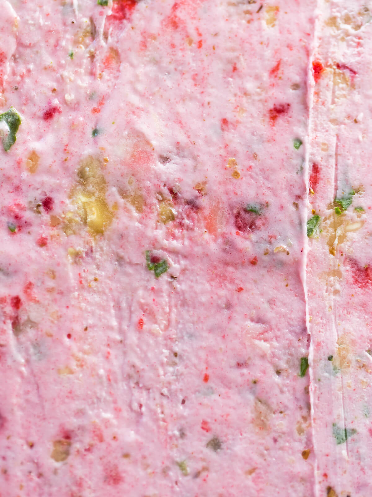 Nahaufnahme der gefrorenen rosa Eisschicht mit eingeschlossenen Erdbeerstücken, Kiwistückchen und grünen Basilikumblättern