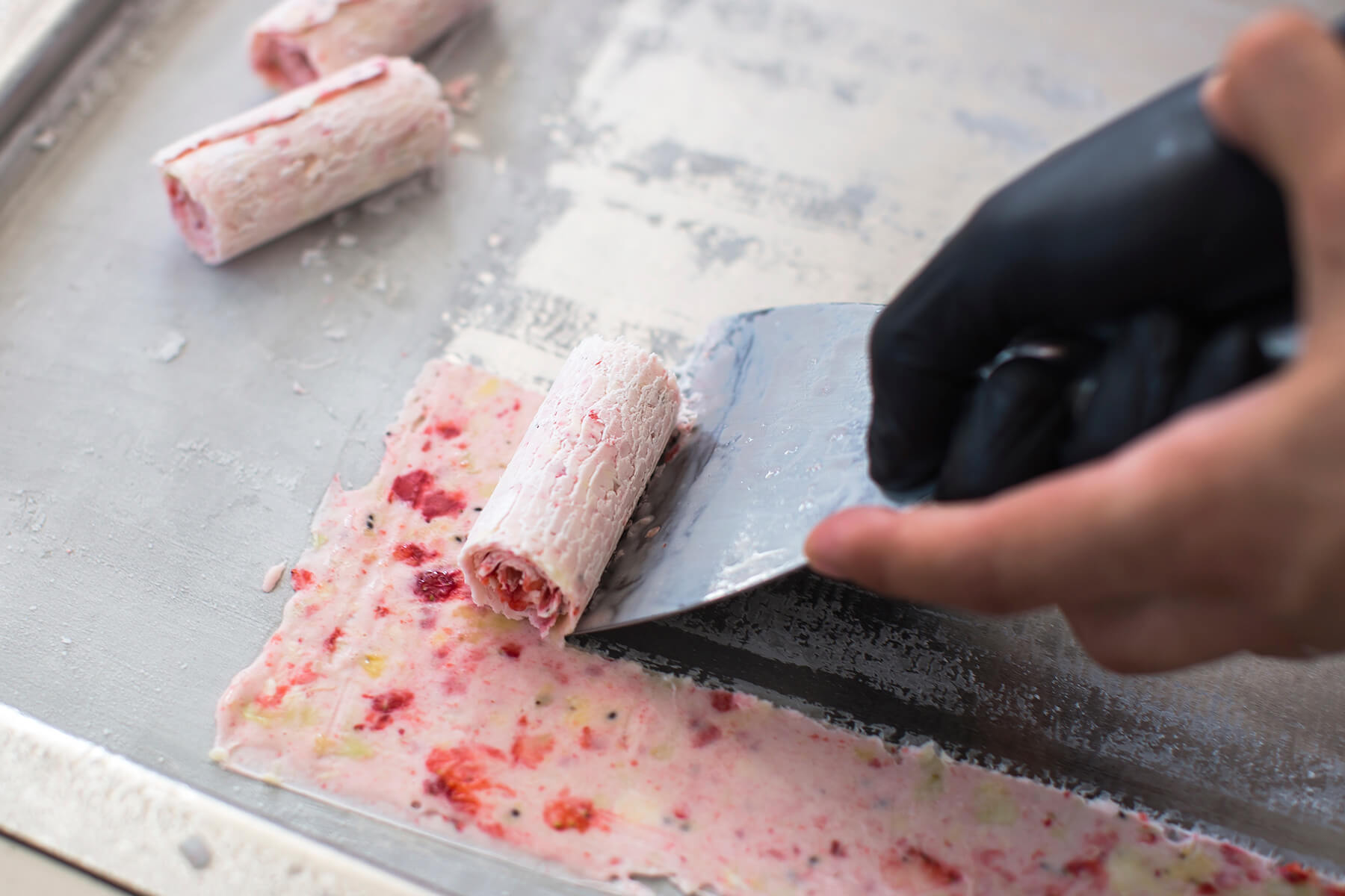 Ein Spachtel schiebt einen Streifen der gefrorenen Eisschicht ab, der sich dabei zu einer Rolle aufwickelt