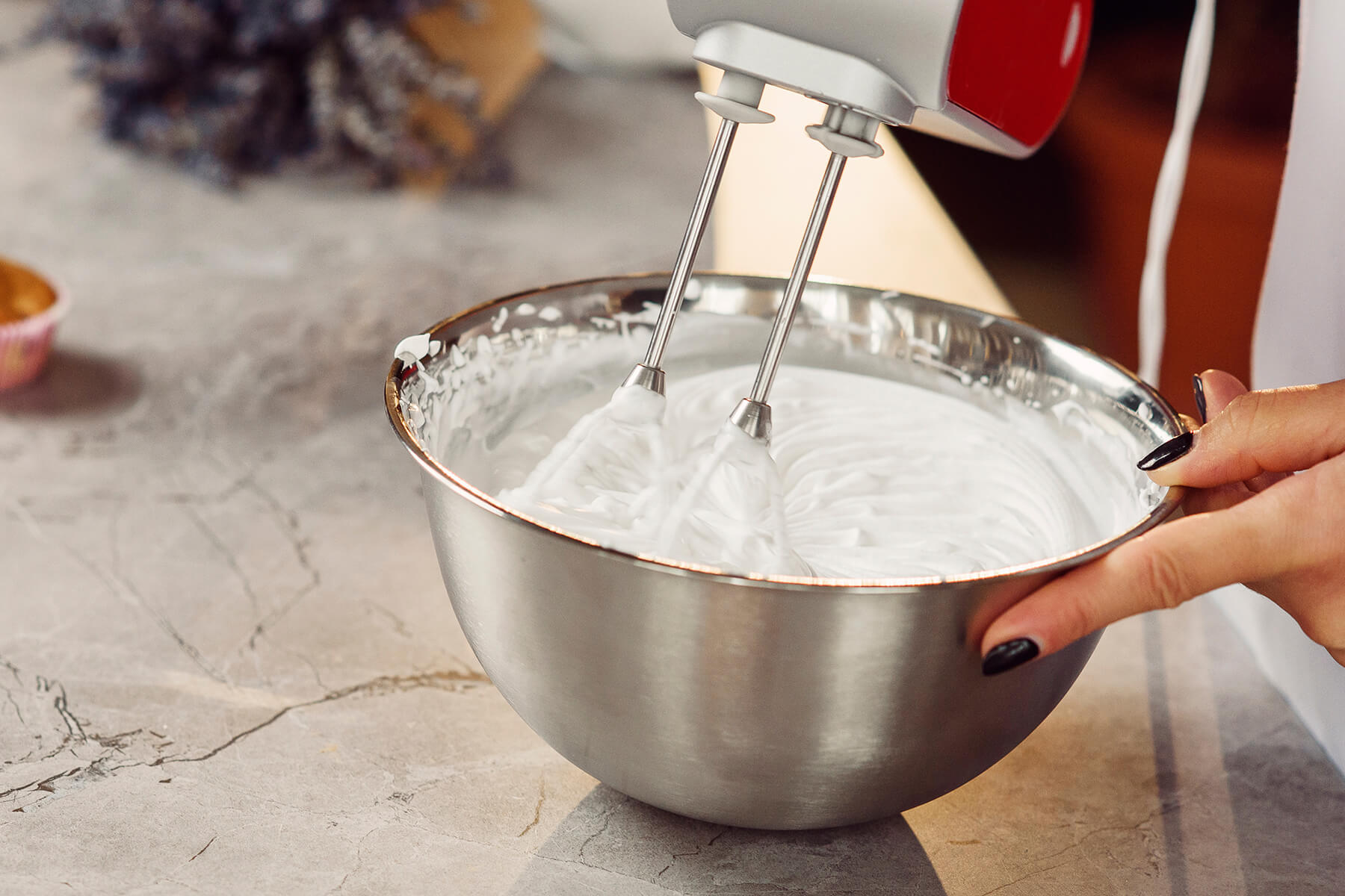 Steif geschlagene weiße Crememasse in einer Edelstahlschüssel, die Quirle des Handmixers hinterlassen stehende Rillen