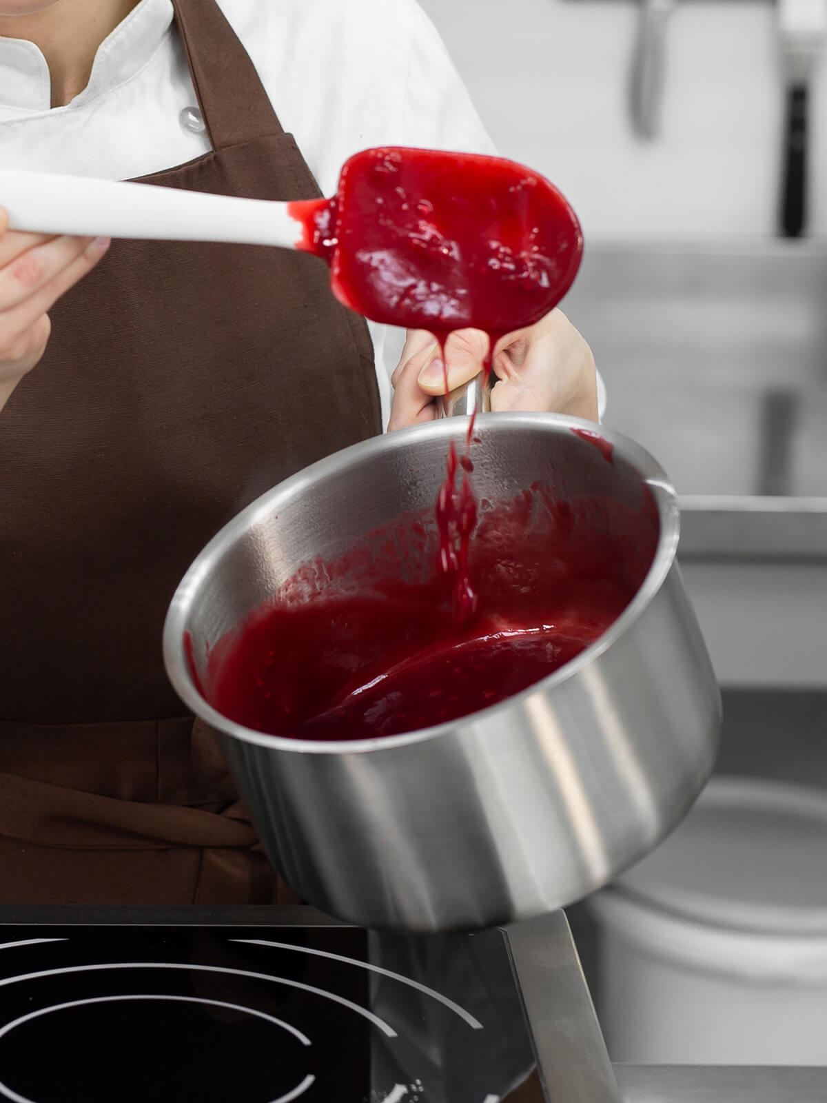 Rote Fruchtmasse fällt in einem breiten Band vom Teigschaber zurück in den Topf