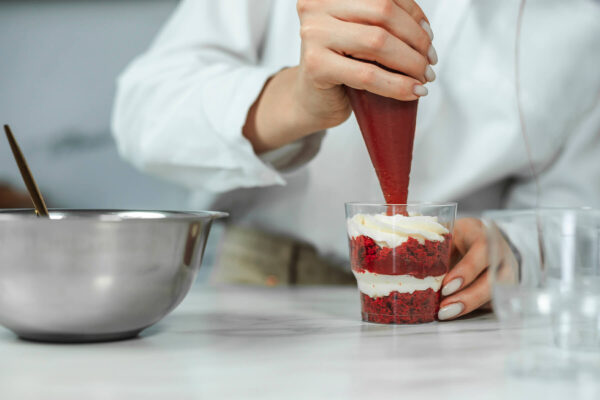 Fruchtpüree wird aus einem Spritzbeutel auf eine Cremeschicht im Dessertglas gespritzt