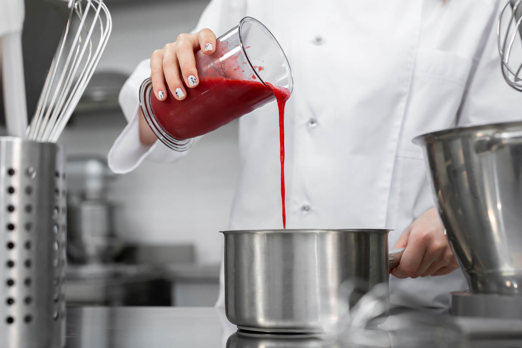 Rotes Fruchtpüree wird aus einem Messbecher in einen Edelstahltopf gegossen