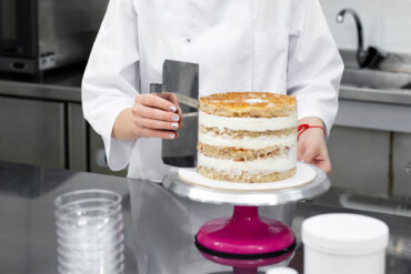 Gefüllte Torte auf einem runden Cakeboard, das auf der Aluminiumplatte eines Drehtellers steht, daneben eine Teigkarte