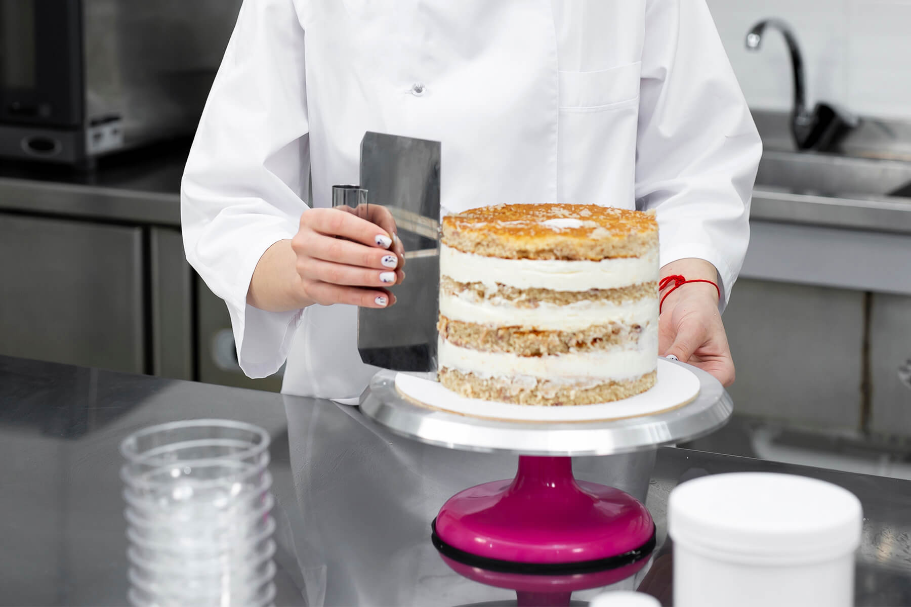 Gefüllte Torte auf einem runden Cakeboard, das auf der Aluminiumplatte eines Drehtellers steht, daneben eine Teigkarte