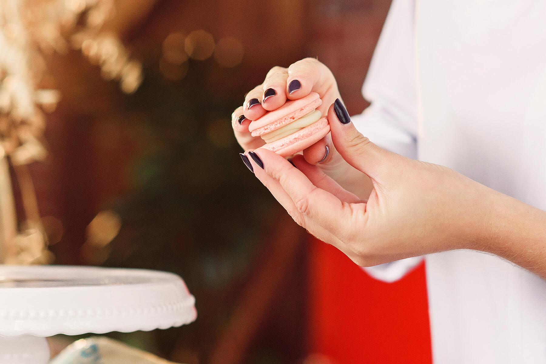 Ein fertiges rosafarbenes Macaron wird zwischen zwei Fingern gehalten, die Cremeschicht ist als klare Fuge sichtbar