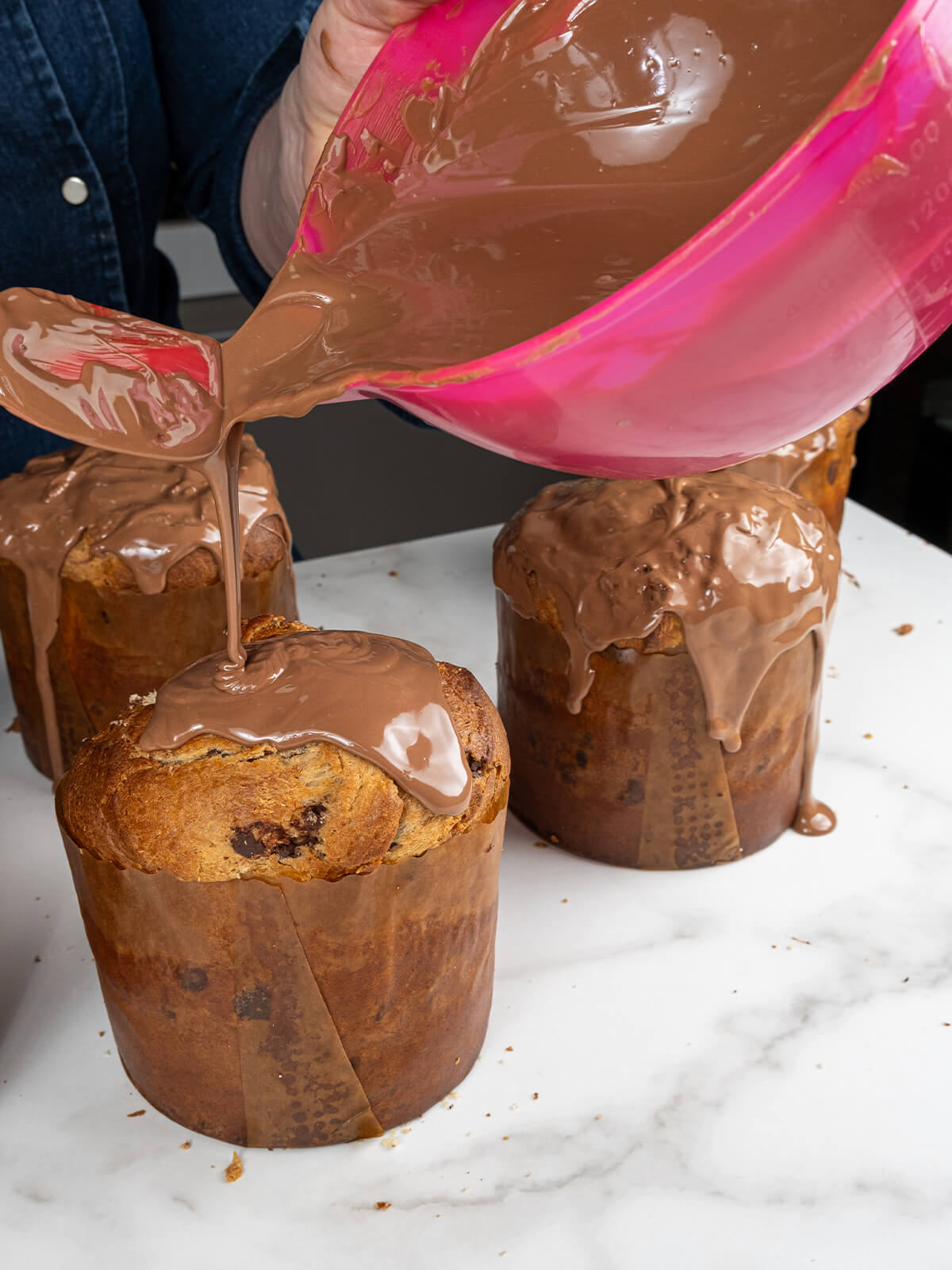 Aus einer pinken Schüssel läuft geschmolzene Milchschokolade über die Deckel mehrerer gefüllter Hefegebäcke