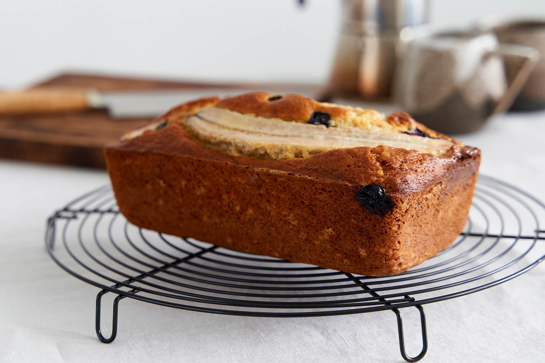Bananenbrot mit Heidelbeeren kühlt auf einem schwarzen Kuchengitter aus, dunkle Beeren zeichnen sich in der Kruste ab