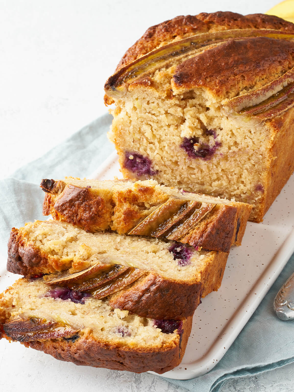 Aufgeschnittenes Bananenbrot mit Heidelbeeren, drei Scheiben liegen vor dem Laib