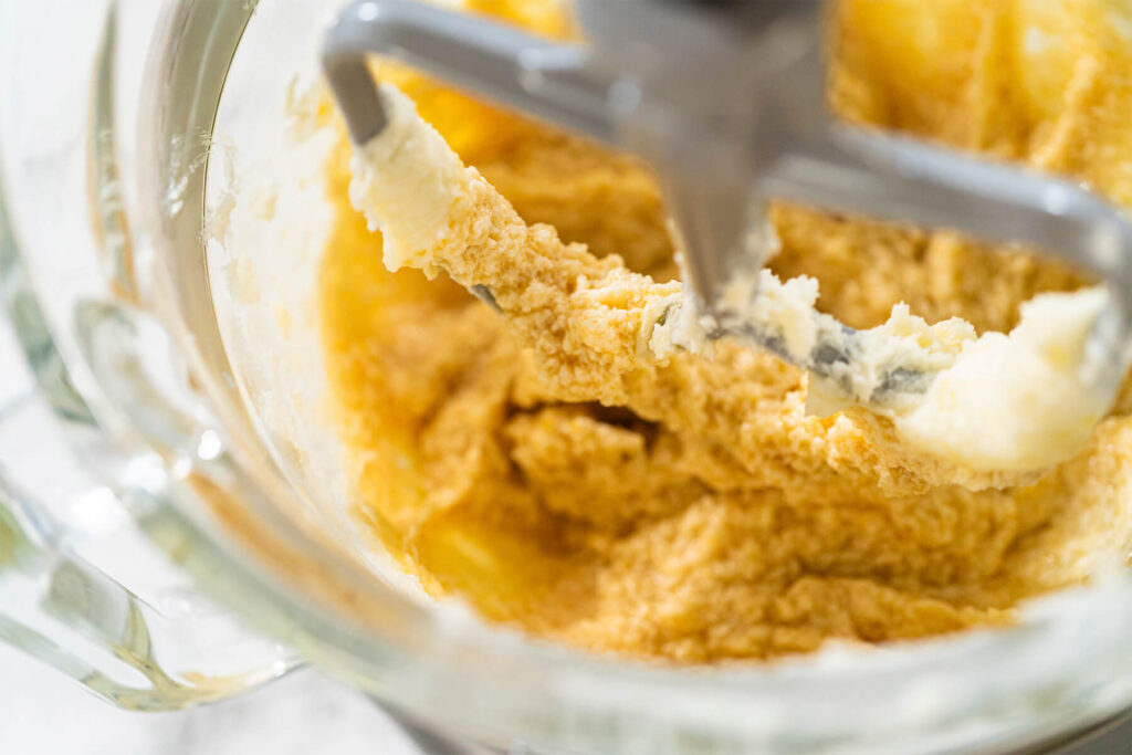 Hell aufgeschlagene Butter-Zucker-Masse mit Ei und noch sichtbaren Butterstückchen in der Glasschüssel der Küchenmaschine