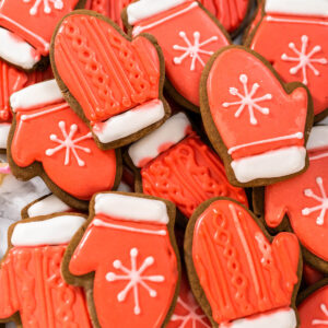 Rot glasierte Lebkuchen-Fäustlinge mit weißer Manschette und weißen Schneeflocken auf mittelbraunem Keksgrund