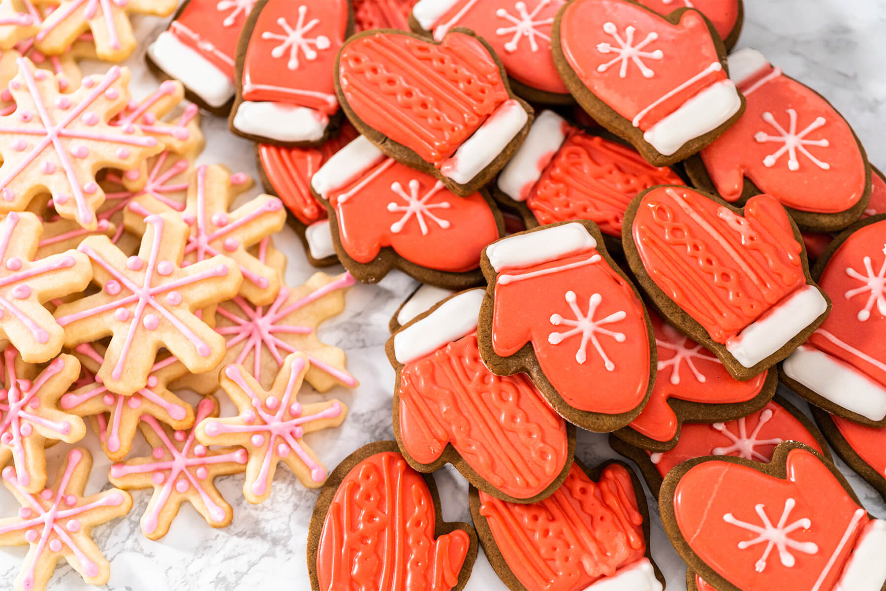 Rot verzierte Lebkuchen-Fäustlinge neben blassen Zuckerkeks-Schneeflocken mit rosa Linien