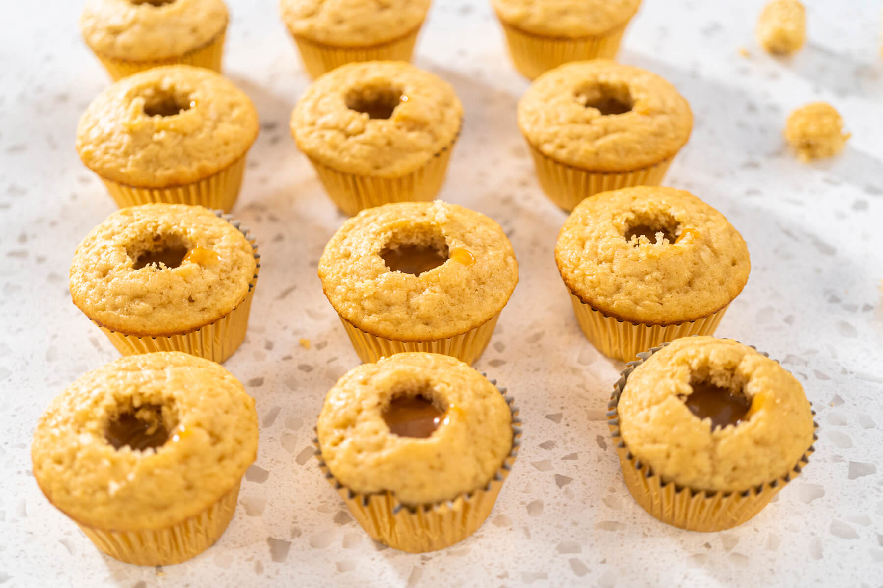 Reihen ausgestochener Karamell-Cupcakes, einige davon bereits mit Karamell gefüllt