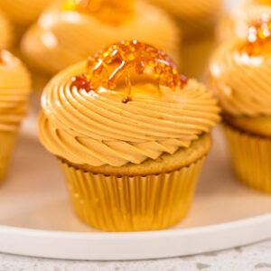 Fertige Karamell-Cupcakes mit Dulce-de-Leche-Creme und bernsteinfarbenem Karamellgitter auf einem weißen Teller