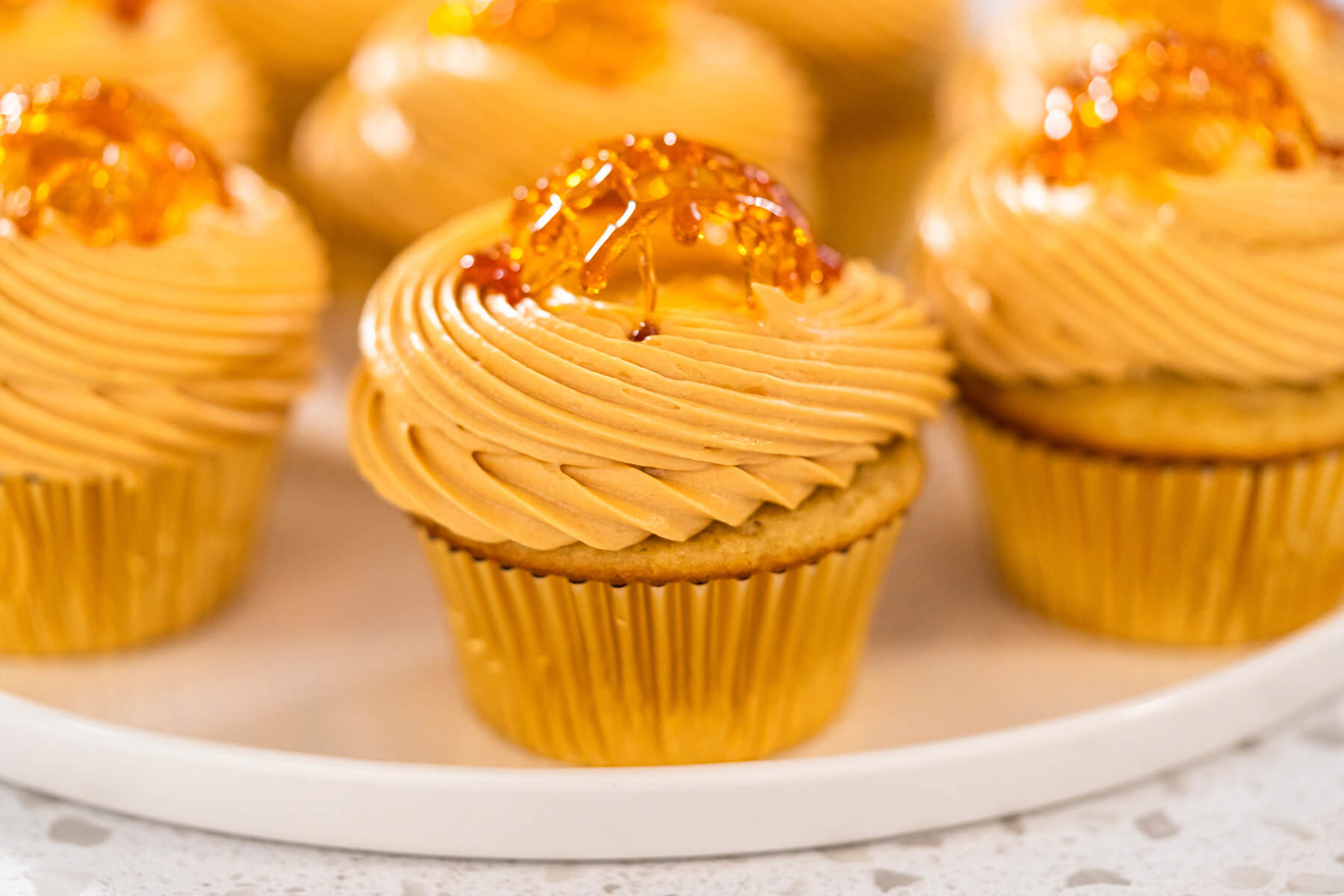 Fertige Karamell-Cupcakes mit Dulce-de-Leche-Creme und bernsteinfarbenem Karamellgitter auf einem weißen Teller