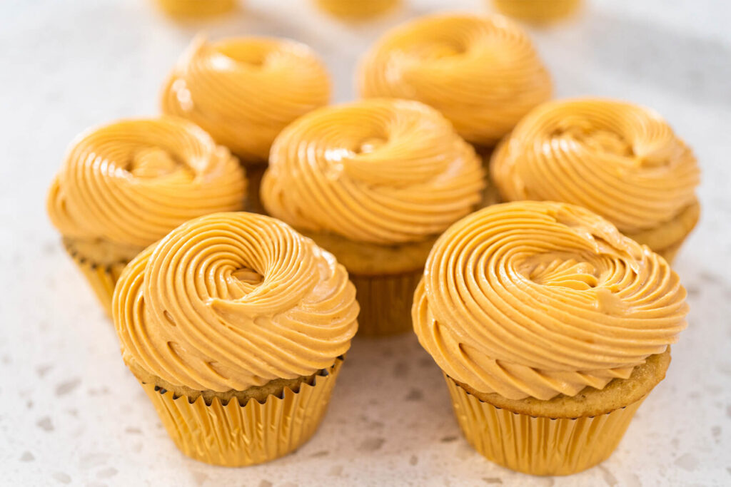 Sieben Karamell-Cupcakes mit aufgespritzten Buttercreme-Rosetten in goldenen Förmchen