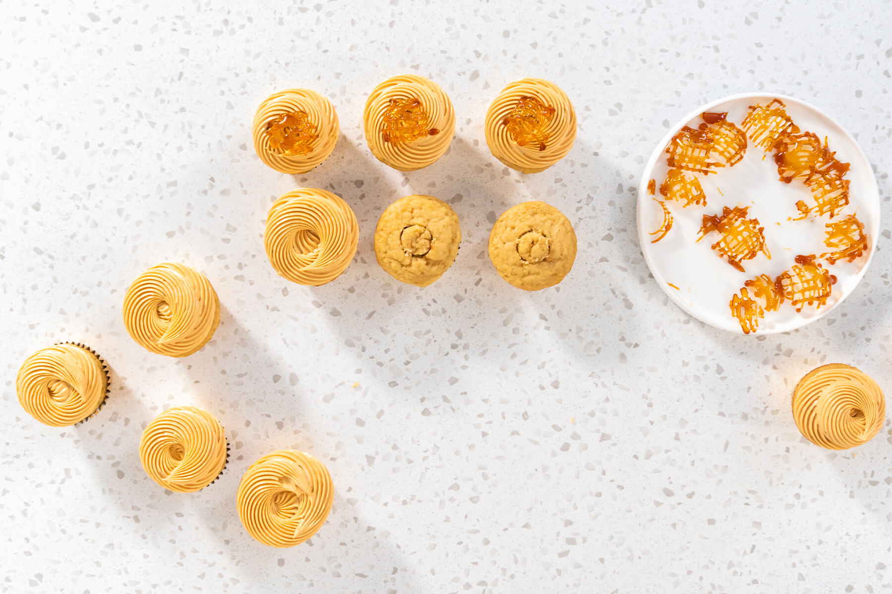 Aufsicht auf verzierte Karamell-Cupcakes, teils mit Karamellgitter, daneben der Teller mit den übrigen Toppern