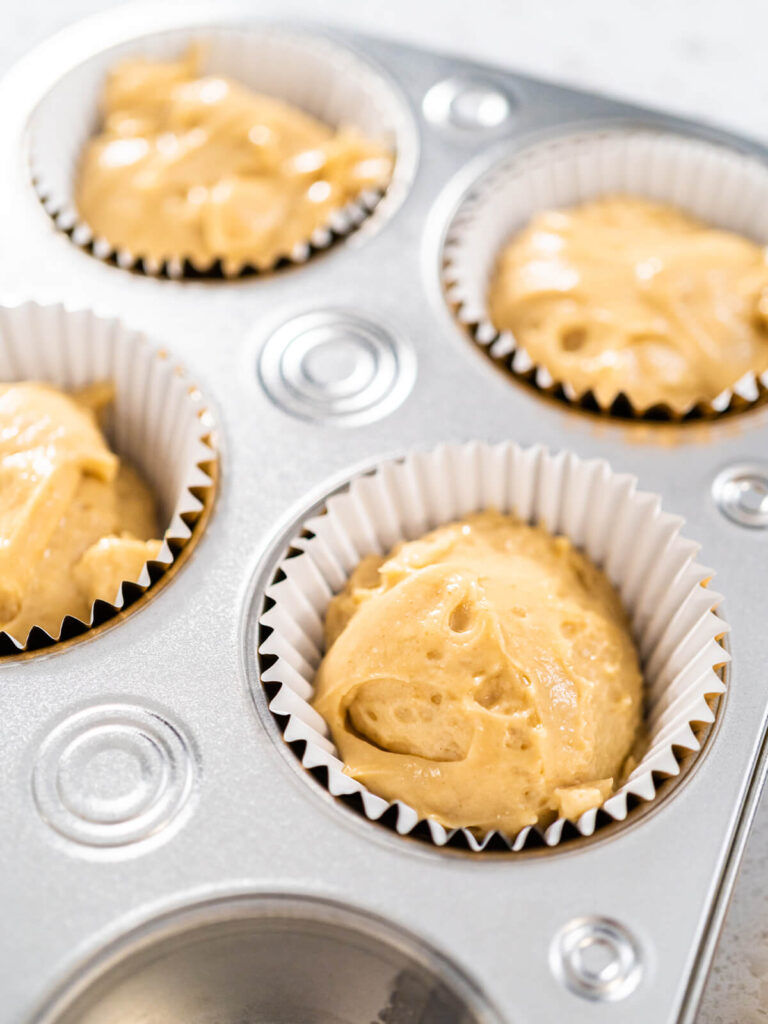 Karamell-Cupcake-Teig zu zwei Dritteln in weiße Papierförmchen im Muffinblech gefüllt