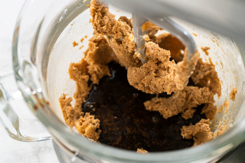 Dunkler Zuckerrübensirup in der Mitte der hell aufgeschlagenen Butter-Zucker-Masse in der Rührschüssel