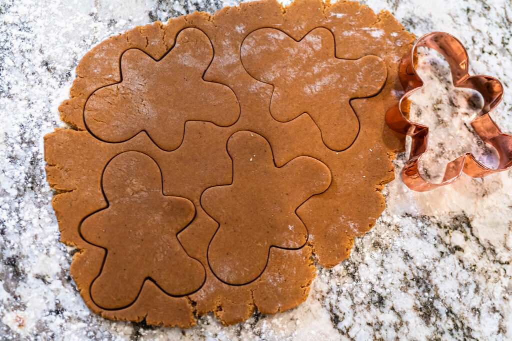Ausgerollter Lebkuchenteig mit vier ausgestochenen Männchen und einer kupfernen Ausstechform auf bemehlter Arbeitsfläche
