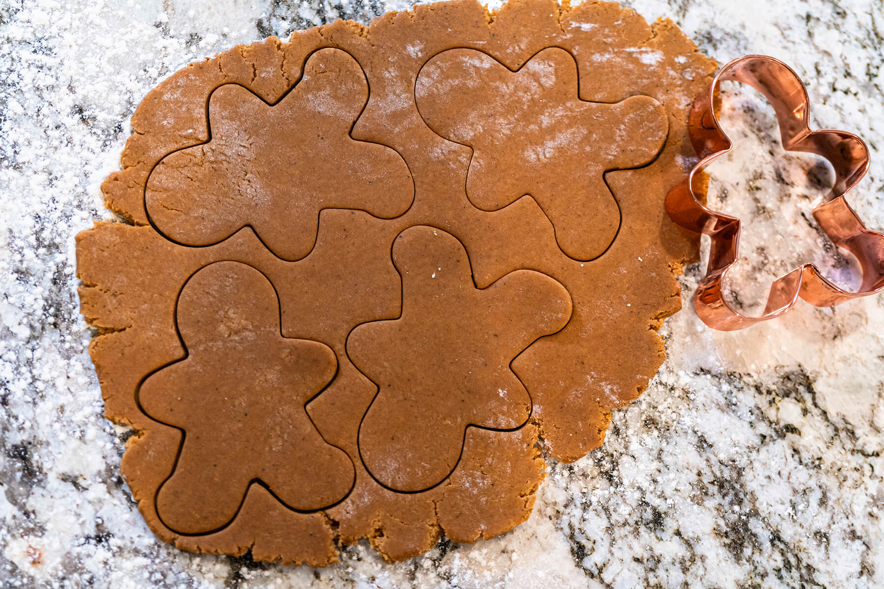 Ausgerollter Lebkuchenteig mit vier ausgestochenen Männchen und einer kupfernen Ausstechform auf bemehlter Arbeitsfläche