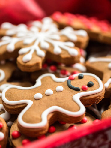 Klassischer Lebkuchen-Mann mit weißer Konturglasur neben einer verzierten Schneeflocke und roten Zuckerperlen