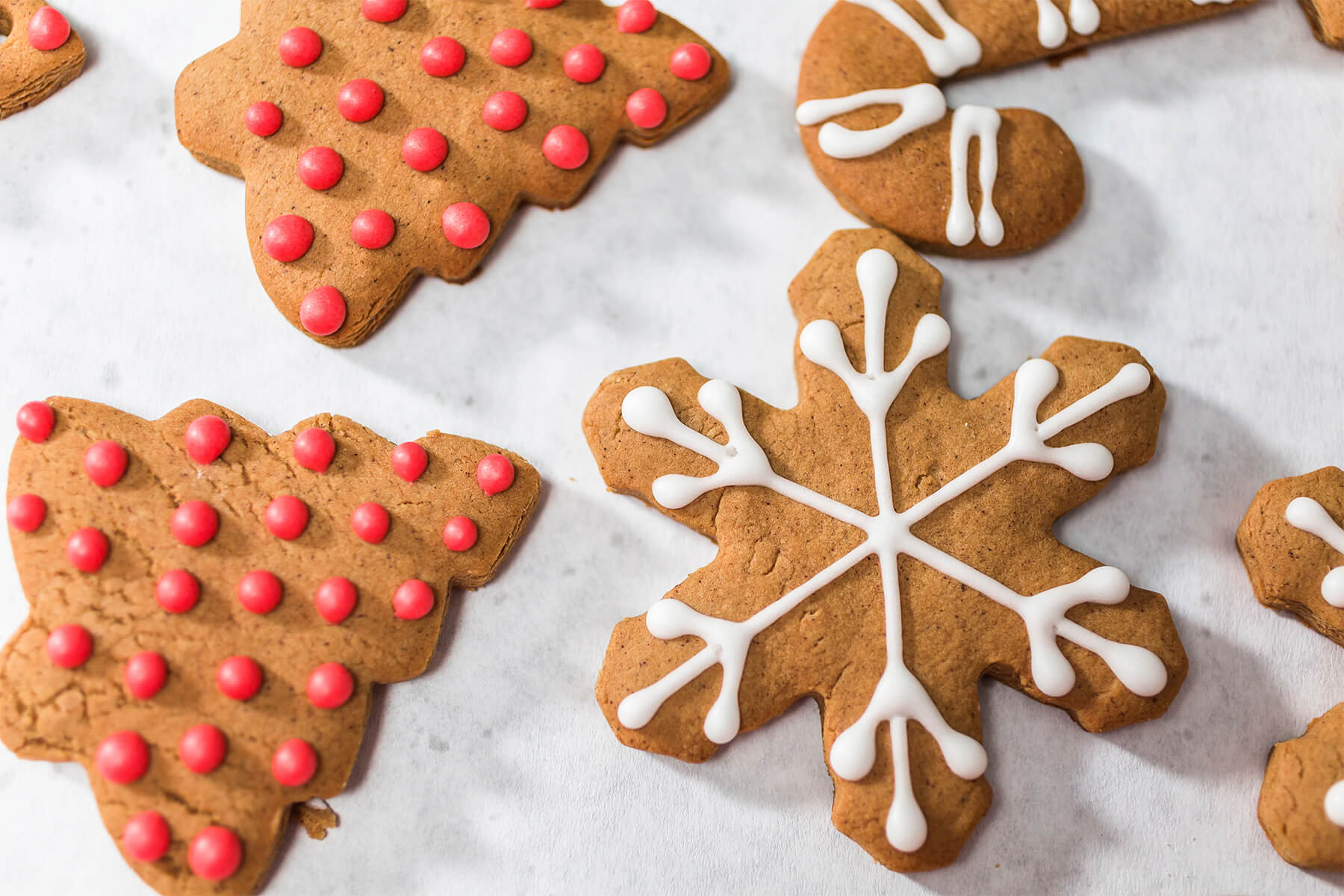 Lebkuchen-Tannen mit roten Zuckerperlen neben einer weiß gespritzten Schneeflocke und einer Zuckerstange