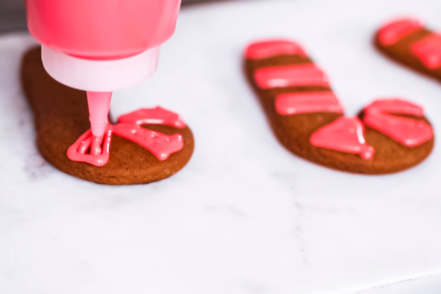 Ein Spritzbeutel setzt rote Eiweißglasur auf einen Lebkuchen in Zuckerstangen-Form