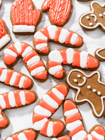 Lebkuchen-Zuckerstangen mit rot-weißen Streifen, ein roter Fäustling und weiß umrandete Lebkuchen-Männchen auf einer Marmorfläche