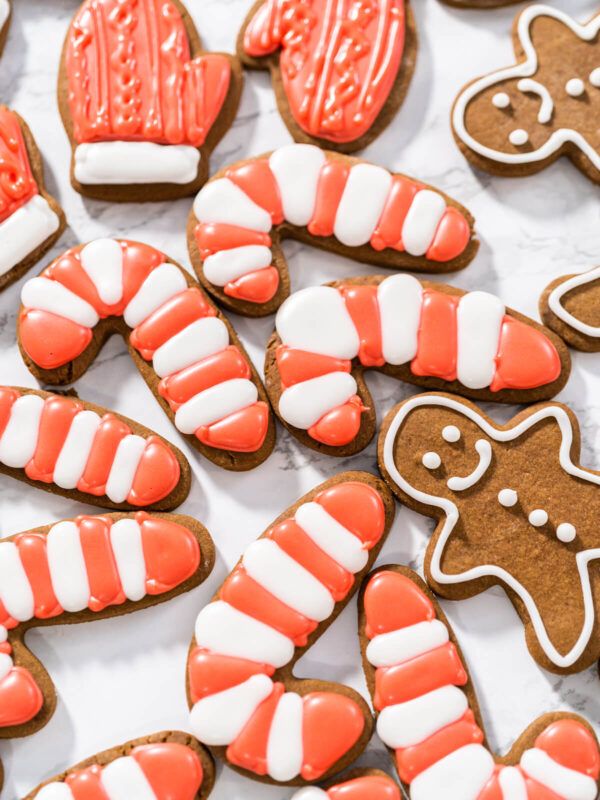 Lebkuchen-Zuckerstangen mit rot-weißen Streifen, ein roter Fäustling und weiß umrandete Lebkuchen-Männchen auf einer Marmorfläche