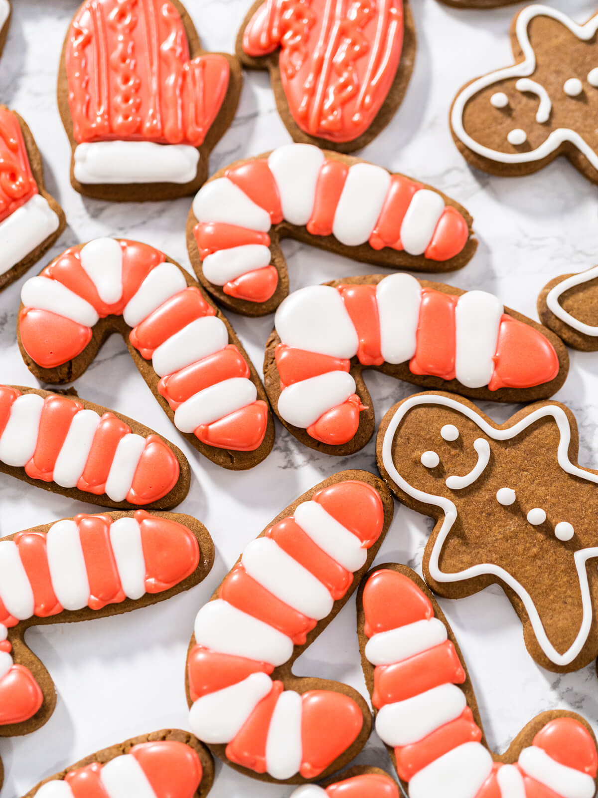 Lebkuchen-Zuckerstangen mit rot-weißen Streifen, ein roter Fäustling und weiß umrandete Lebkuchen-Männchen auf einer Marmorfläche