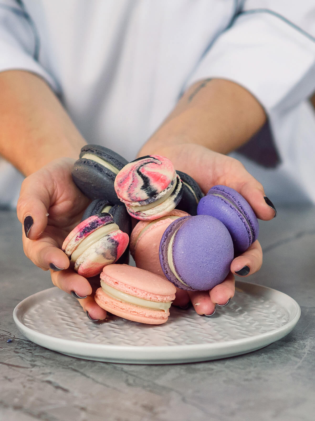 Zwei Hände halten einen Haufen Macarons, darunter mehrere marmorierte mit jeweils unterschiedlichem Muster