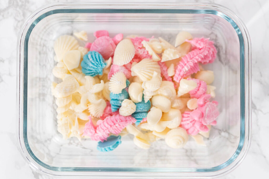 Glasdose mit fertigen Schokoladenfiguren: weiße Muscheln, rosa Seepferdchen und blau schimmernde Muscheln nebeneinander