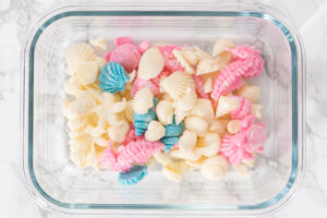 Glasdose mit fertigen Schokoladenfiguren: weiße Muscheln, rosa Seepferdchen und blau schimmernde Muscheln nebeneinander