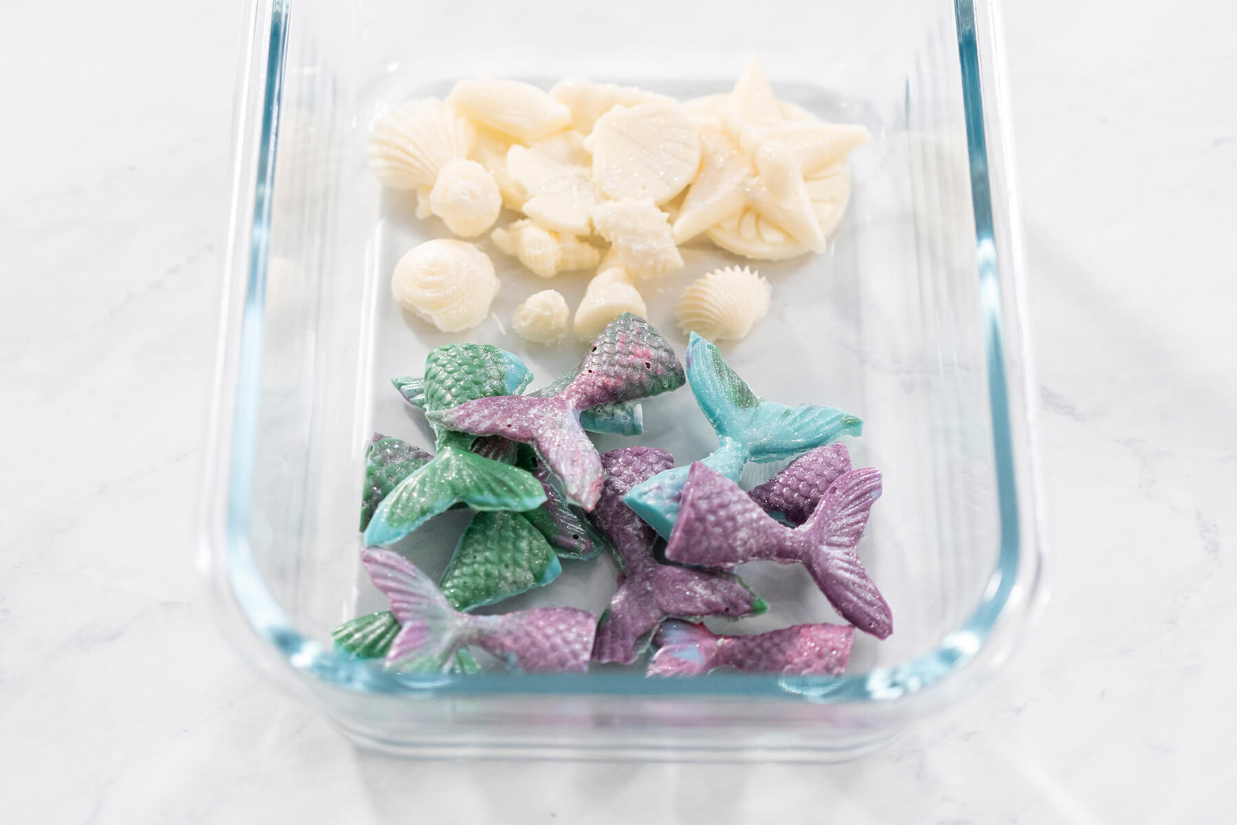 Vorratsdose aus Glas mit weißen Schokoladenmuscheln und marmorierten Meerjungfrauen-Flossen in Grün, Türkis und Violett
