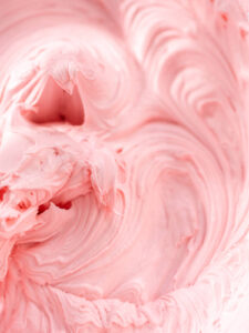 Nahaufnahme fein aufgeschlagener rosa Buttercreme mit weichen Wirbeln und glänzender Oberfläche