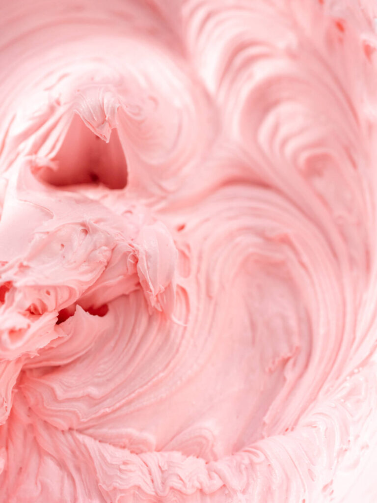 Nahaufnahme fein aufgeschlagener rosa Buttercreme mit weichen Wirbeln und glänzender Oberfläche