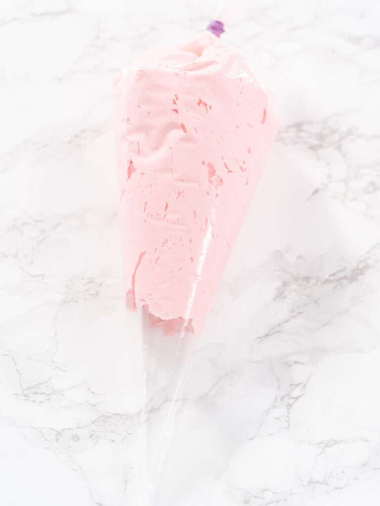 Spritzbeutel gefüllt mit rosa Buttercreme, oben mit einem Clip verschlossen, auf heller Marmorfläche