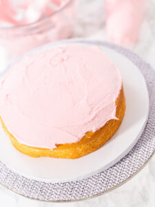Erster goldbrauner Vanilleboden auf einer weißen Kuchenpappe, gleichmäßig mit rosa Buttercreme bestrichen