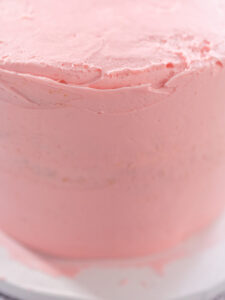 Gestapelte Torte rundherum mit einer dünnen rosa Krümelschicht aus Buttercreme eingestrichen, Nahaufnahme