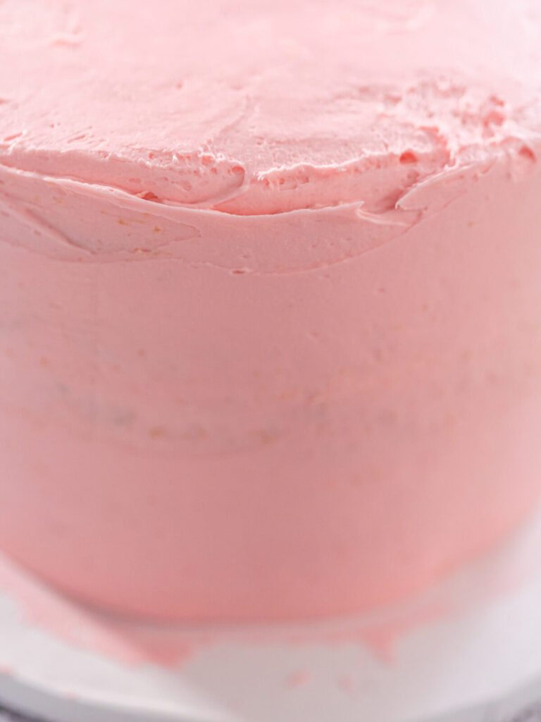 Gestapelte Torte rundherum mit einer dünnen rosa Krümelschicht aus Buttercreme eingestrichen, Nahaufnahme