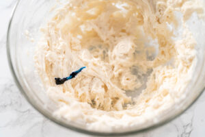 Weiße Buttercreme in einer Glasschüssel, auf die ein Tropfen blaues Lebensmittelgel gegeben wurde