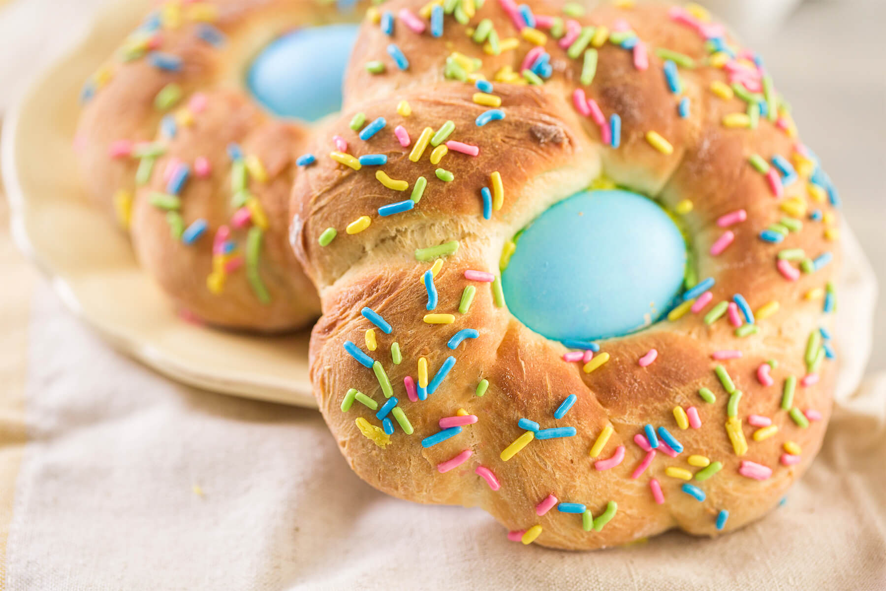 Zwei gebackene Mini-Osterbrote mit hellblauen Eiern und bunten Zuckerstäbchen nebeneinander auf einem hellen Teller