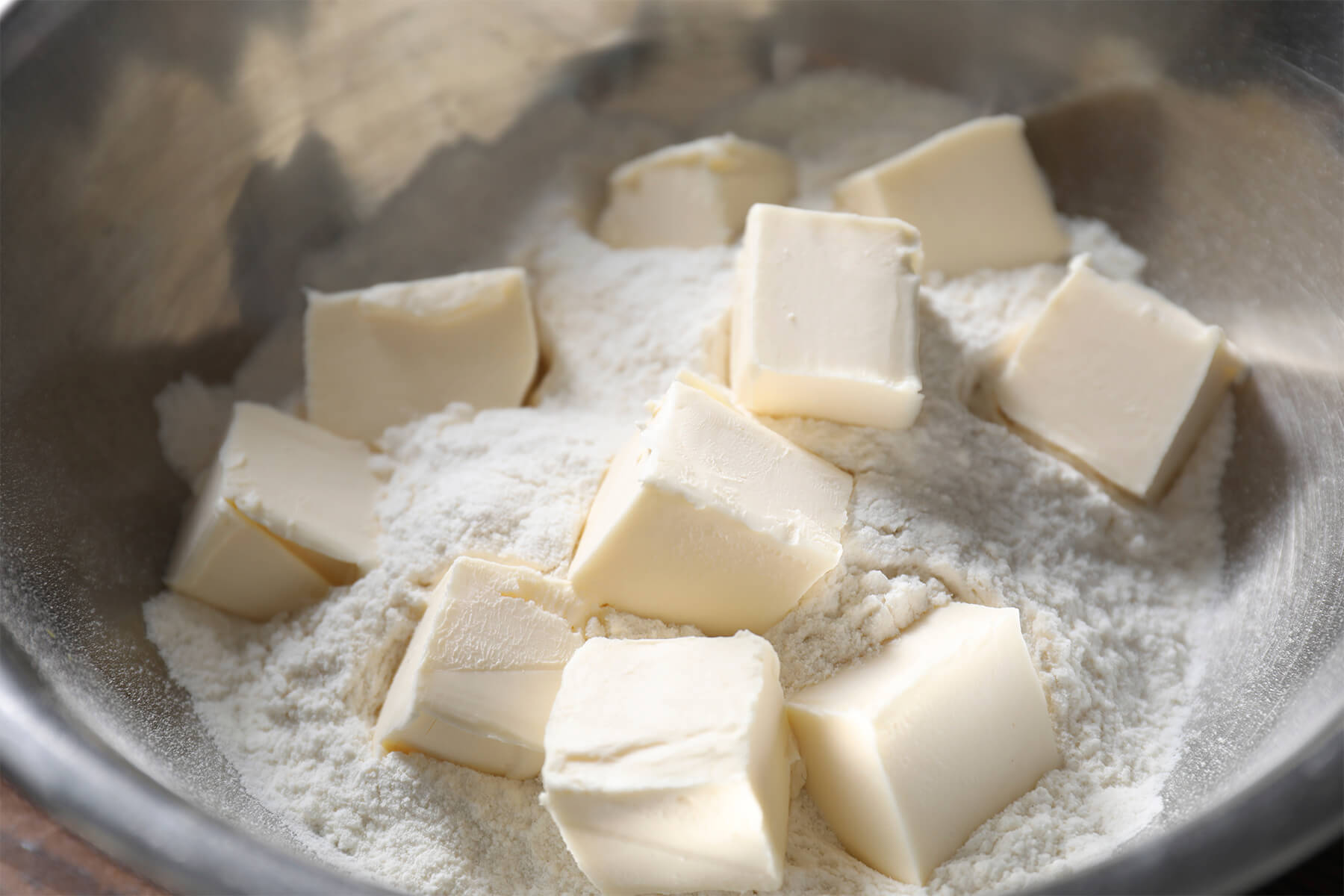 Kalte Butterwürfel auf Mehl in einer Metallschüssel, bereit für Mürbeteig
