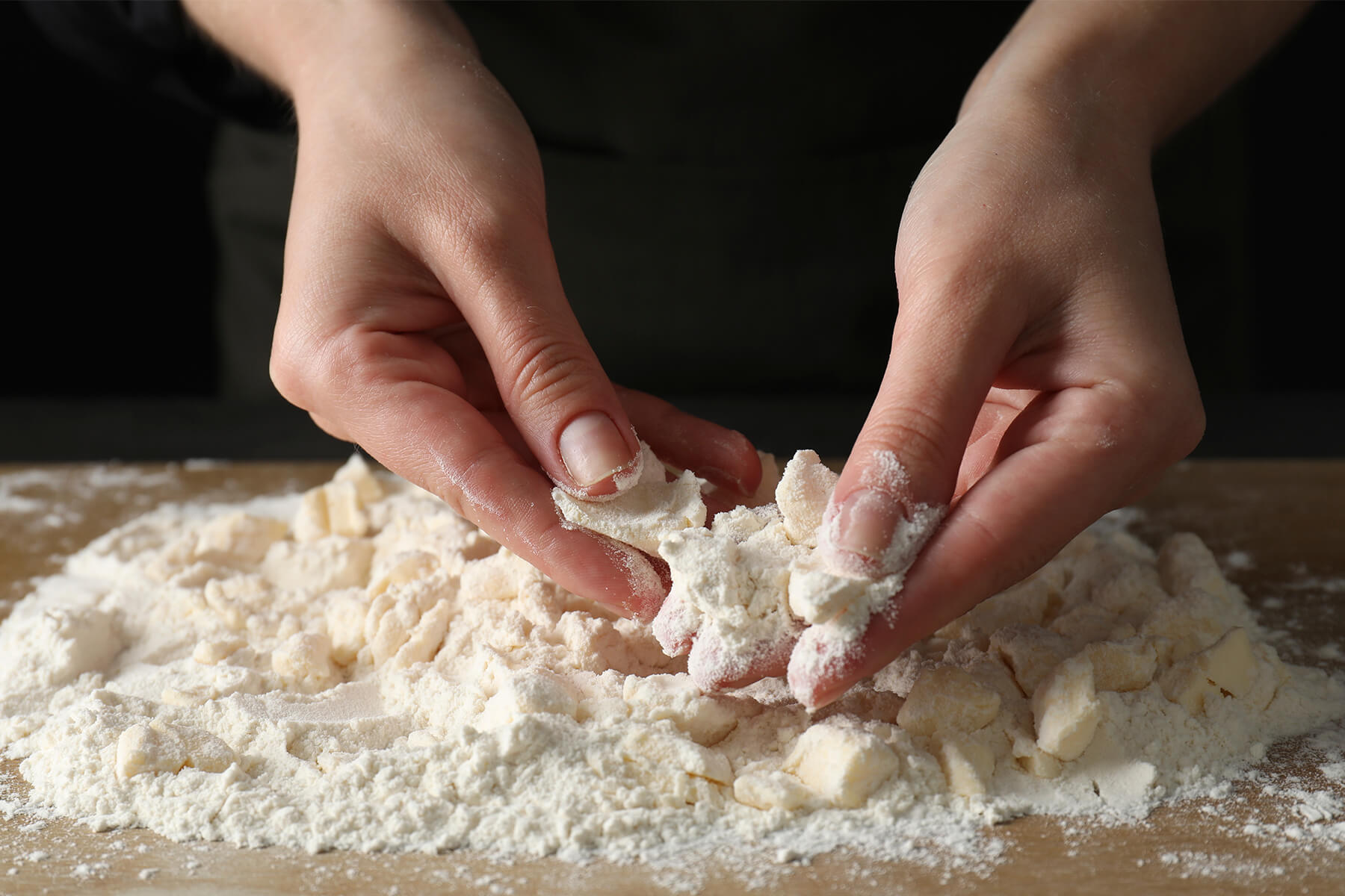 Hände reiben kalte Butter zu groben Krümeln in das Mehl auf einem Holzbrett ein