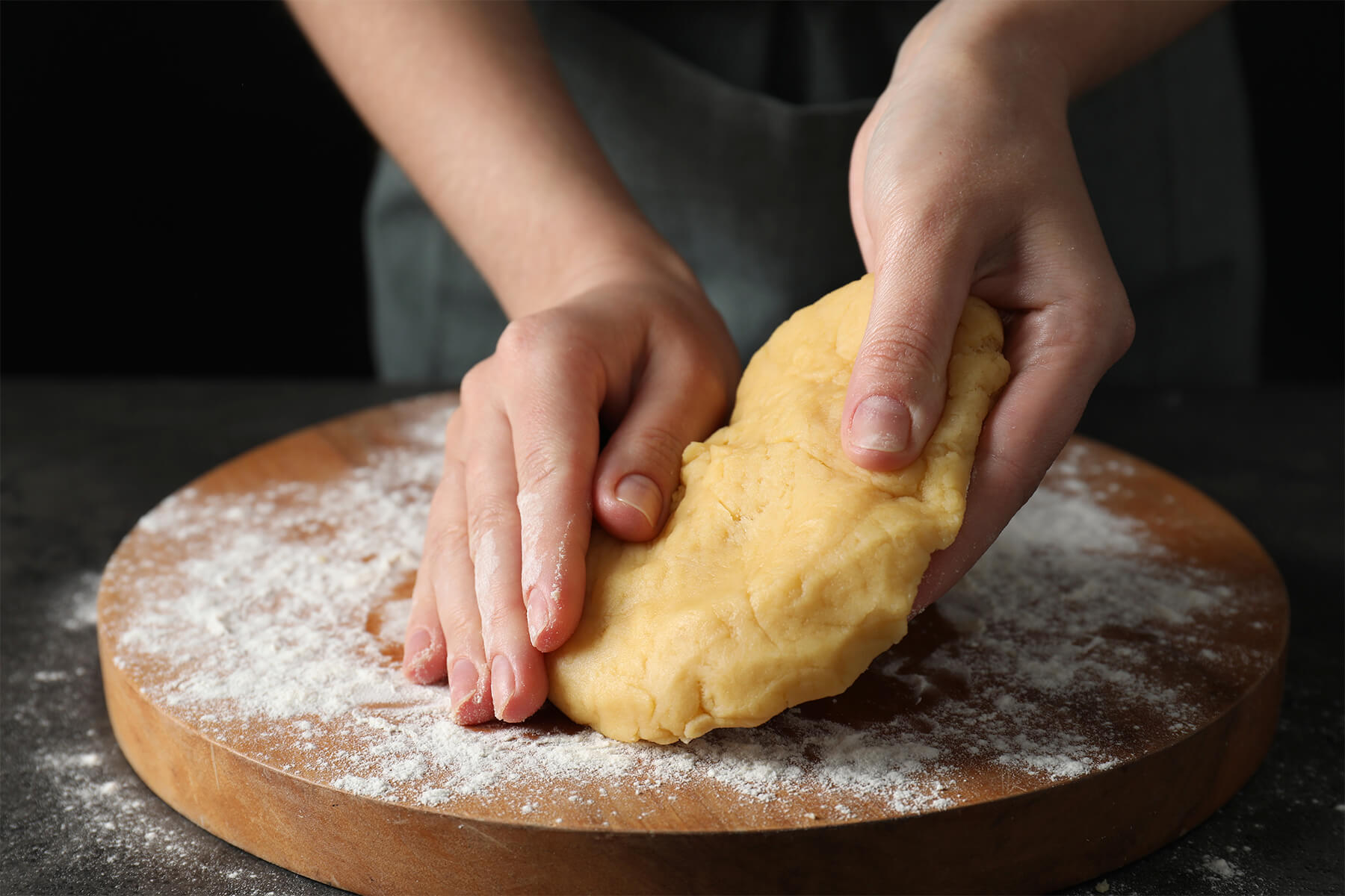 Hände fügen gelben Mürbeteig auf einem bemehlten Holzbrett rasch zu einer Kugel zusammen