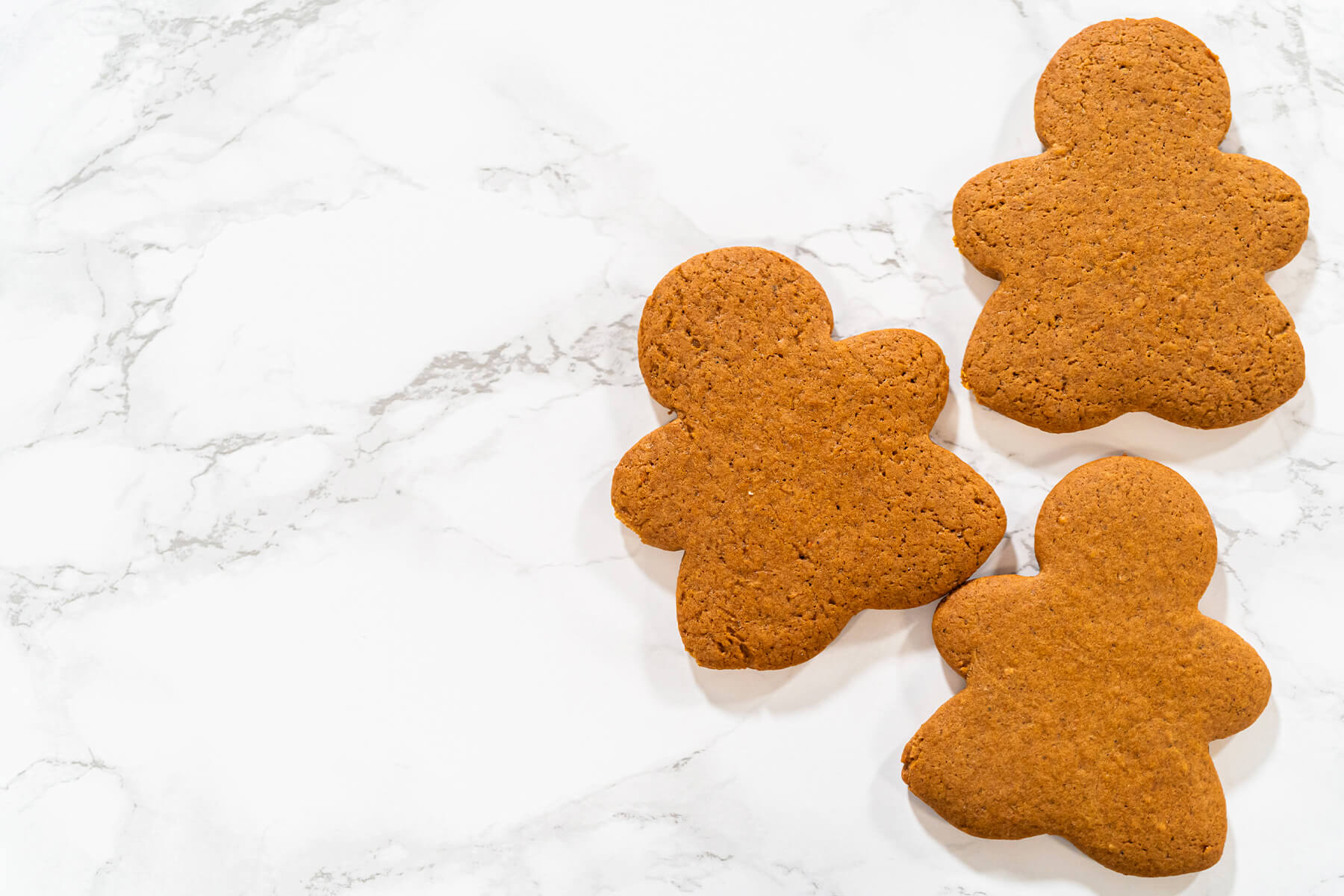 Drei gebackene Lebkuchen-Figuren in warmem Braun auf einer hellen Marmorfläche