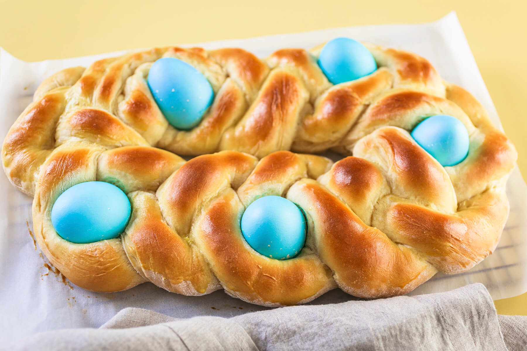 Gebackenes geflochtenes Osterbrot als längliches Oval mit fünf blau gefärbten Eiern auf einem hellen Backpapier