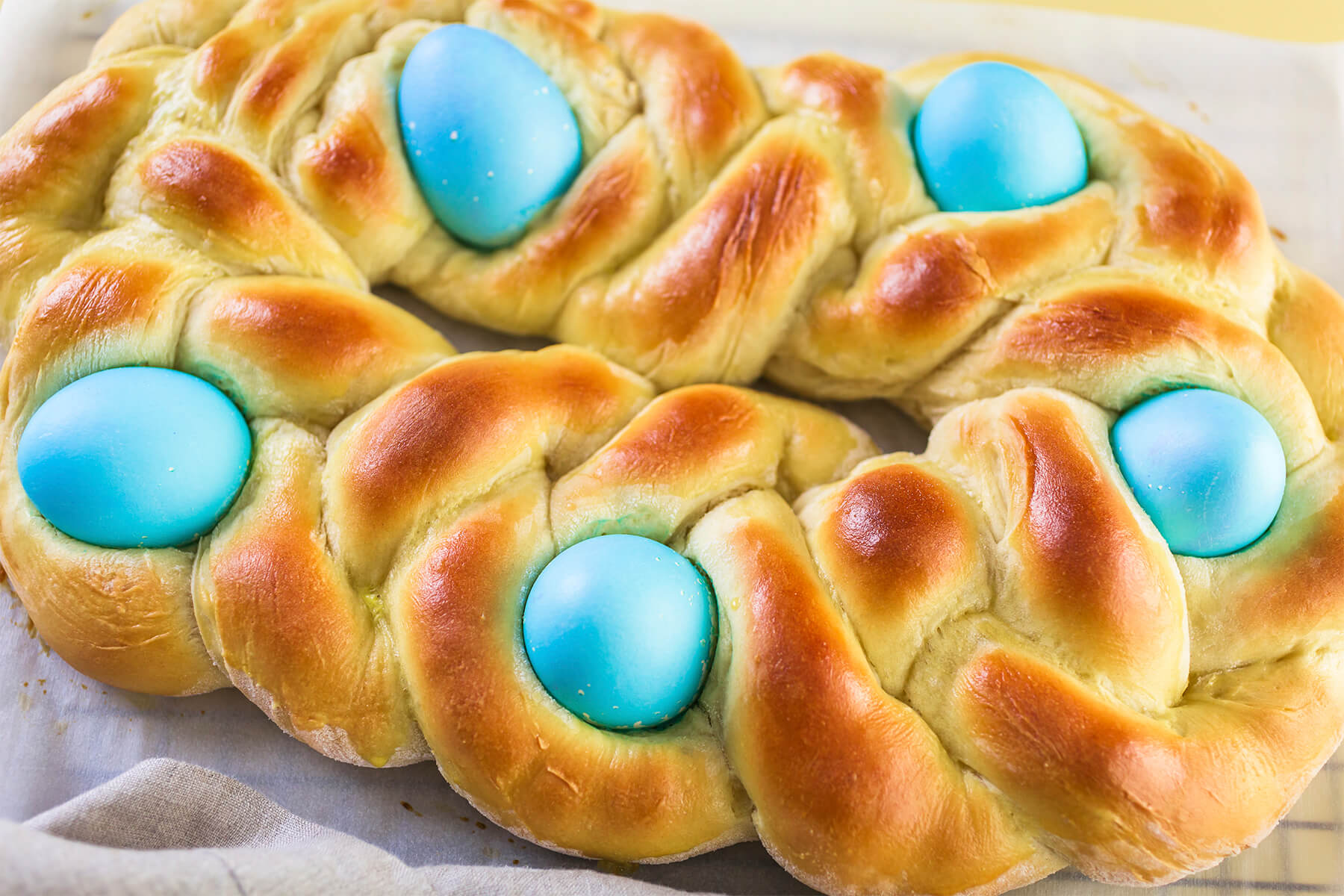 Gebackenes geflochtenes Osterbrot in Nahaufnahme, die drei Stränge deutlich erkennbar, dazwischen vier blau gefärbte Eier