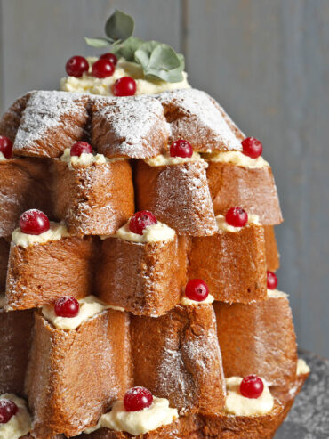 Nahaufnahme eines Pandoro-Baums mit gelblichen Cremetupfen in jeder Zackenlücke, roten Beeren darauf und dickem Puderzucker