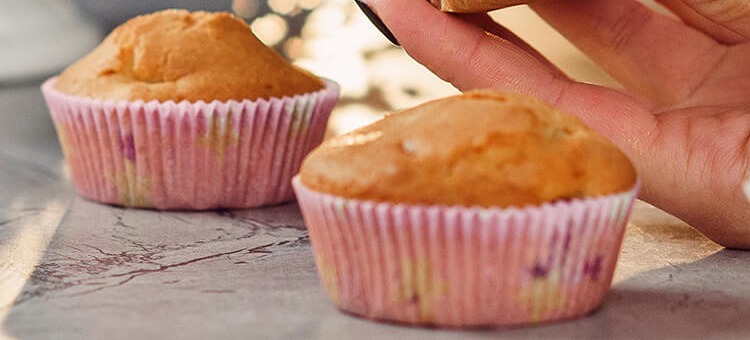 Zwei Muffins in rosa gemusterten Papierförmchen, deren untere Hälfte durchscheinende Fettflecken und violette Verfärbungen zeigt